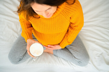 Top-down view of pregnant woman in lotus position holding latte, contemplating dietary choices...