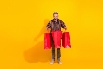 Cheerful man holding red shopping bags on vibrant yellow background shows joy and excitement while highlighting retail and fashion