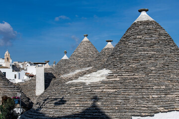 Close up of characteristic conical stone roofs of Trulli houses with the city of Albarobello,...
