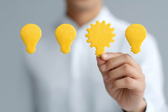 A person holds a bright yellow light bulb shape, symbolizing ideas and creativity, with additional bulb shapes displayed nearby.