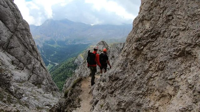 Two lone hikers navigates a steep rocky ledge along the Colac via ferrata, framed by sharp cliffs in Trentino&rsquo;s Dolomites.