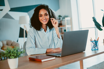 Young woman working on a laptop in a stylish home office setting with natural daylight, showcasing...