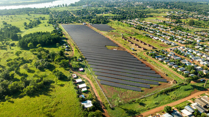 Aerial view of a solar energy farm in San Javier, Misiones, Argentina, surrounded by rural houses, green fields, and the river in the background.