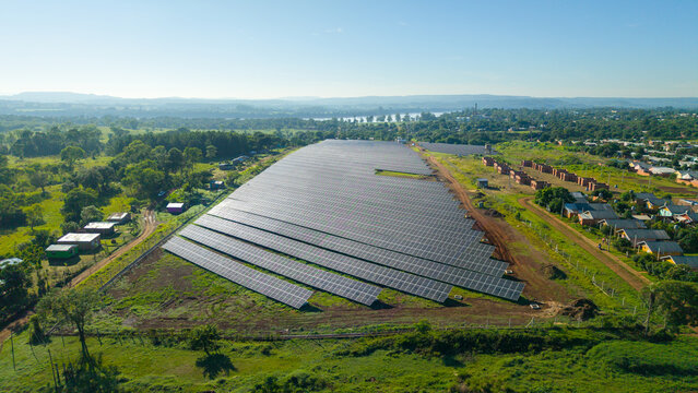 Aerial view of a solar power plant in San Javier, Misiones, Argentina, located near a rural village and surrounded by lush green landscape and distant hills.