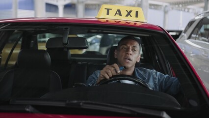 Young taxi driver smoking an e-cigarette while driving car in the city. People, job, health concept.