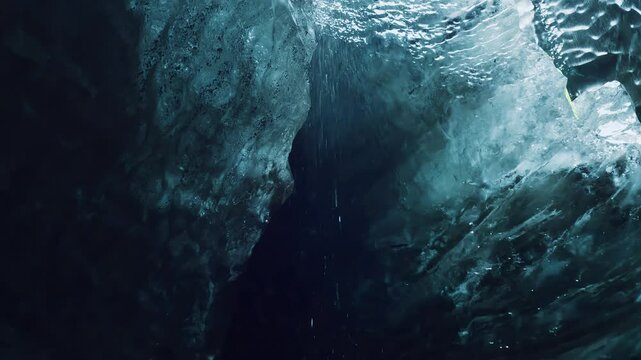 Explorer checking global warming in glacier cave in Iceland with trapped ash inside the ice, water dripping from melting ice