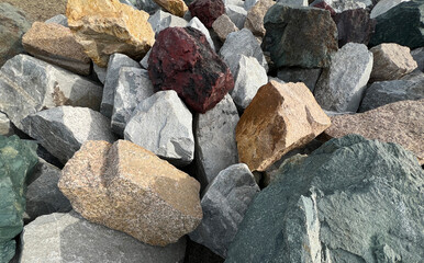 Assortment of variously colored rocks closely arranged outdoors, natural textures and hues - grey, brown, red, and green stones for geological observation