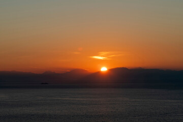 Panoramic view during sunrise over the Tyrrhenian Sea with the Amalfi coastline, Italy coloring orange in early morning light and one ship silhouette on water