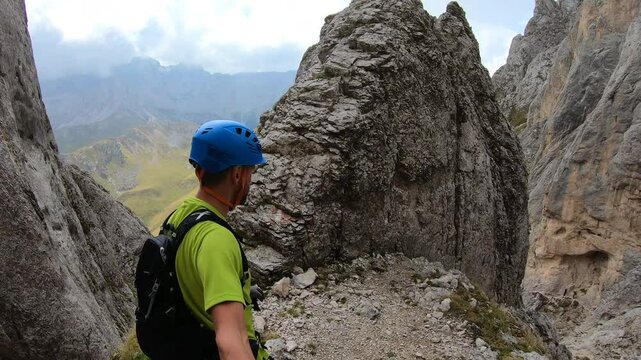 A hiker walks at a high mountain pass on the Finanzieri route, gazing over the Trentino peaks under a soft blue sky.