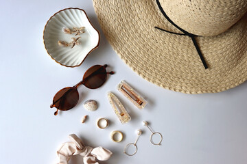 Sunglasses, straw hat, shells and jewelry in neutral colors. Seasonal summer accessories on white background. Flat lay.