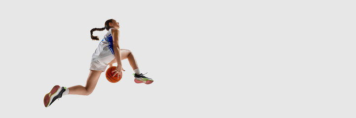 Banner. Focused young athlete girl, basketball player performing slam dunk in motion against white...