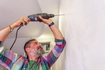 Handyman using a power drill to create a hole in a white wall, engaging in home renovation and DIY...