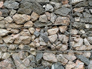 macro photo of gabion wall texture with rough stones in metal mesh, industrial natural background for architectural designs