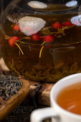 tea with red rose , red rosehip fruits and hot green tea in a transparent teapot