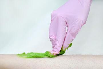 A cosmetologist wearing pink latex gloves removes leg hair. Sugar hair removal foot skin care with liquid sugar. A cosmetologist waxes women's legs at the spa. Female waxing. Epilation by sugaring
