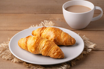 Freshly baked croissants served with a hot cup of coffee on a wooden table in a cozy setting