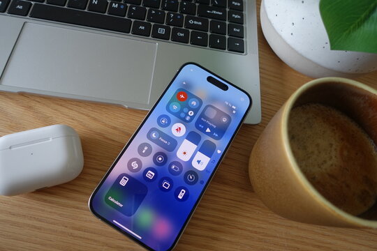 Kiel, SH, Germany, 04-24-2025: Close-up of an iPhone 15 Pro on a wooden desk alongside a laptop and coffee cup, showing the control center interface with airplane mode enabled