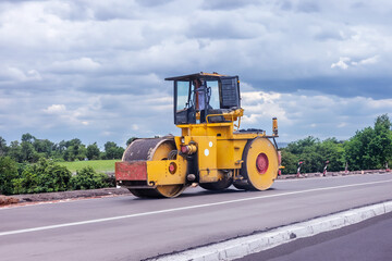 large construction roller moves along an asphalt road.