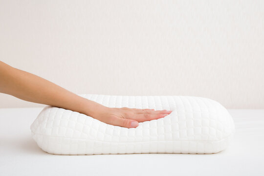 Young adult woman hand touching clean white orthopedic memory foam pillow on mattress. Checking hardness and softness. Closeup. Front view.