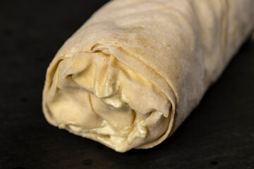 shawarma from thin tortilla with meat with tomatoes and sauce, fast food made from various ingredients packed in foil, closeup