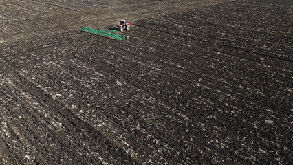 Obraz premium A red tractor works on a plowed field in spring, Russia farming