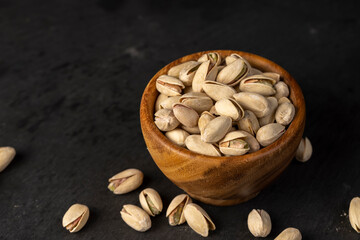 pistachio in their shells with added salt, fried unpeeled pistachio nuts in a wooden bowl with...