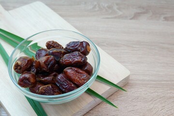 Glass Bowl of Fresh Dates with Tropical Leaves on Wooden Background
