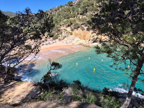 Tourists enjoying summer vacation on aiguablava beach with transparent turquoise water, surrounded by cliffs and green trees, in begur, costa brava, catalonia, spain