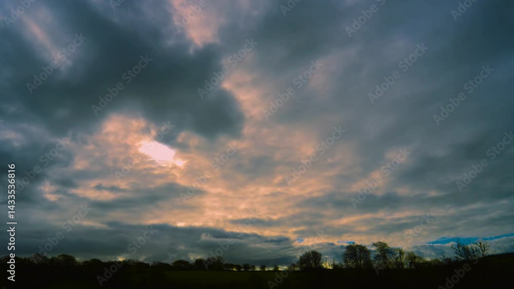 Poster landscape view of fast moving timelapse with bright sunlight behind clouds with trees silhouetted on
