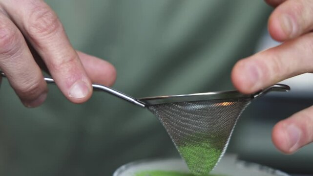 barman making a cocktail using fine strainer.close up bartender hands sprinkle matcha over.restaurant or cafe interior, night club, weekend mood.
