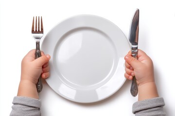 Child's hands grasping fork and knife excitedly before an empty plate ready for a meal on a clean white surface