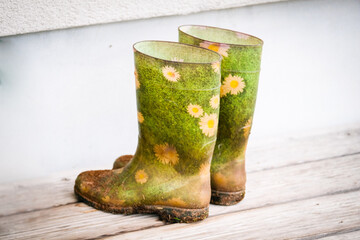 A pair of rubber boots with an artistic design featuring green grass and yellow daisies, placed on...