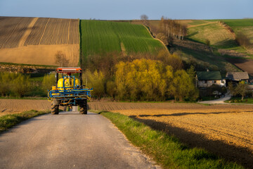 tractor returning from spraying crops, fields, golden hour, earth, blooming trees in spring colors,...