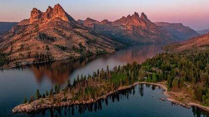 Obraz premium Aerial view of a serene lake nestled among rocky mountains at sunset. The water reflects the warm, golden light, and a small island with trees is visible in the foreground.