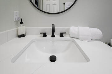 A bathroom sink counter displays a soap bottle, neatly folded towel, and face cloth