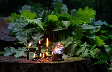 Burning candles, quartz crystal ball, fern and oak leaves in forest, nature background. ritual with...
