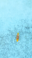 Obraz premium woman in a bikini relaxes on a yellow kayak floating on clear turquoise sea, top-down view from above, peaceful moment in tropical paradise, summer holiday, maldives, travel, holidays, vacation