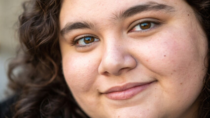 Close up portrait of young person with curly hair and warm brown eyes, expressing gentle smile