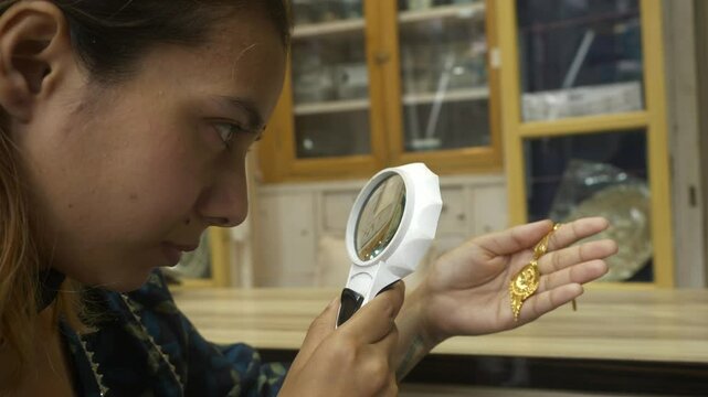 Indian woman checking 18k HUID certified gold jewellery with a magnifying glass at gold shop
