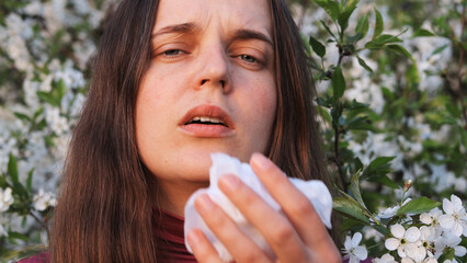 A woman experiences allergy discomfort while surrounded by blooming flowers, capturing the essence...