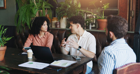 Business, people and discussion with laptop in cafe for startup management, budget planning or feedback. Remote work, teamwork and documents in meeting for financial review, collaboration or strategy