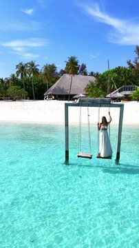 woman swings above the crystal clear sea on a wooden swing facing the beach and lush tropical backdrop, peaceful and carefree moment in maldives, summer holiday, island retreat 05.04.25 Baa Maldives