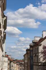 view of the street, hill with building in old style, old street with blue sky with clouds, colors - white, blue, brown