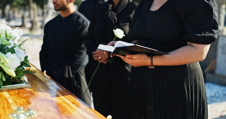 Bible, flower and hands by coffin at funeral for respect, blessing or spiritual comfort at...