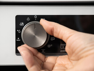 Woman adjusting modern white oven in kitchen.  Female hand pushing and turning knobs on oven...