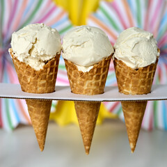 Three waffle cones filled with homemade vanilla ice-cream, on a colorful summer themed background....