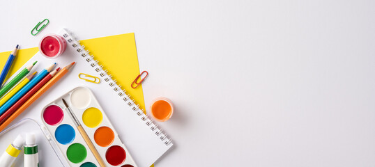 Creative tools arrangement including watercolors, colored pencils, and paper on white background