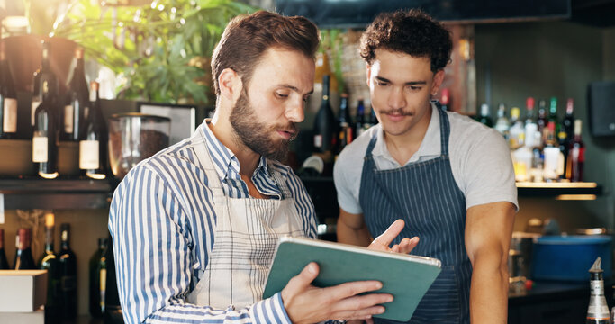 Men, barista and tablet with discussion at cafe with sales report, coach and review schedule at diner. People, mentor and digital touchscreen with app for inventory, menu and training at coffee shop