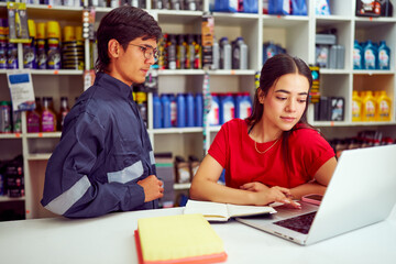Saleswoman using laptop with mechanic looking in auto parts store