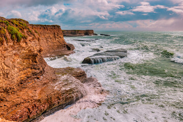 Coastal cliffs along California's Highway 1 in California. Rugged ocean rocks, crashing waves, and a colorful sky create a breathtaking Pacific Coast landscape
